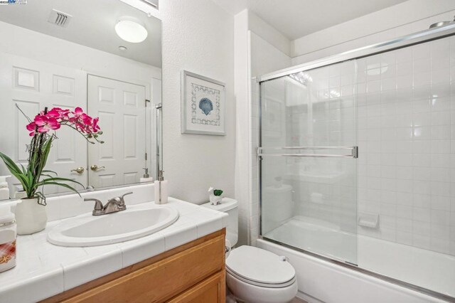 full bathroom featuring toilet, bath / shower combo with glass door, and vanity