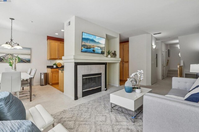 living room featuring a tiled fireplace, light colored carpet, and an inviting chandelier