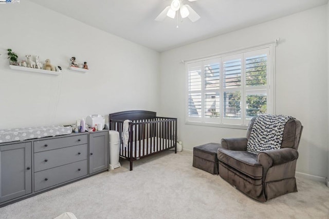 bedroom featuring ceiling fan, a crib, and light carpet