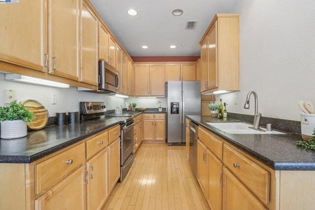 kitchen featuring light hardwood / wood-style flooring, sink, appliances with stainless steel finishes, dark stone countertops, and light brown cabinets