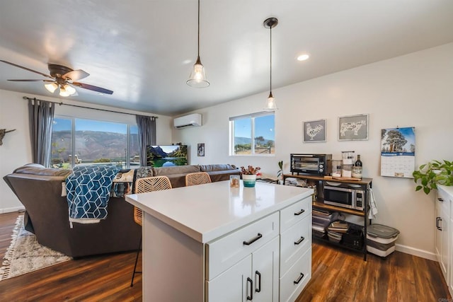 kitchen featuring an AC wall unit, white cabinets, a center island, decorative light fixtures, and a breakfast bar