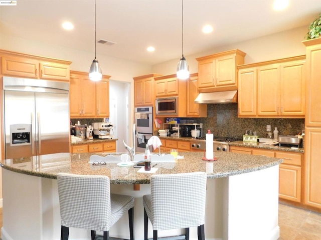 kitchen with extractor fan, a kitchen island with sink, hanging light fixtures, light stone countertops, and built in appliances