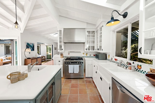 kitchen featuring white cabinets, appliances with stainless steel finishes, wall chimney exhaust hood, decorative light fixtures, and vaulted ceiling with beams