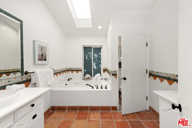 bathroom featuring tile patterned flooring, tiled tub, vanity, a skylight, and toilet