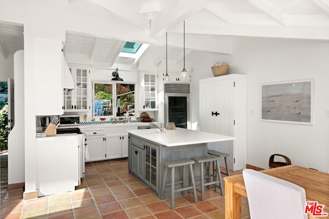 kitchen with an island with sink, decorative light fixtures, vaulted ceiling with skylight, white cabinets, and sink