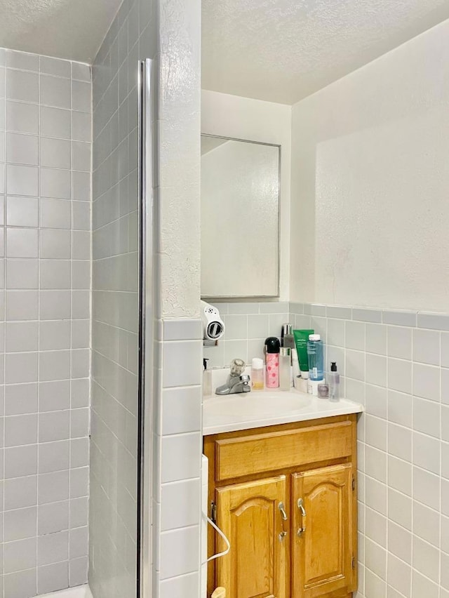 bathroom featuring a textured ceiling, a shower with door, vanity, and tile walls