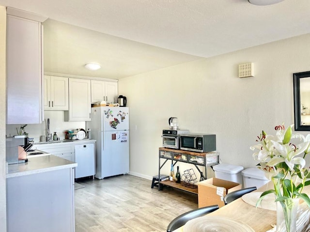 kitchen featuring sink, white cabinets, light hardwood / wood-style floors, and white appliances