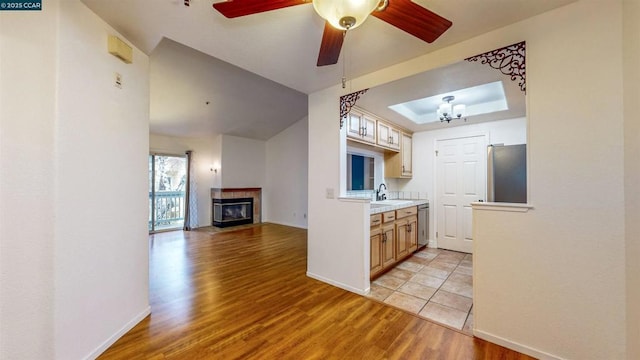 kitchen featuring a fireplace, a tray ceiling, light hardwood / wood-style flooring, stainless steel appliances, and ceiling fan with notable chandelier