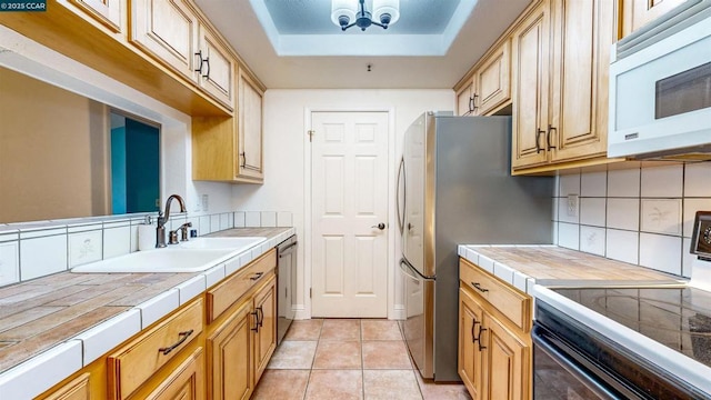 kitchen featuring sink, a tray ceiling, appliances with stainless steel finishes, tile counters, and light tile patterned floors