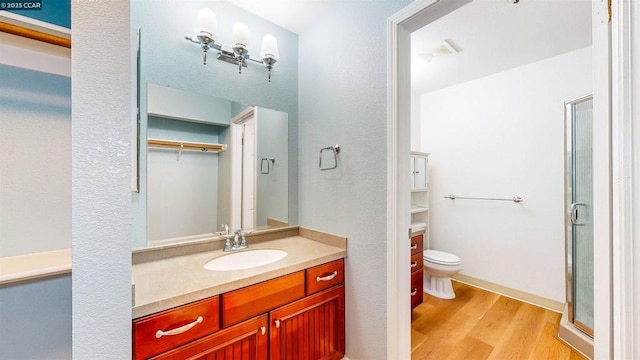 bathroom featuring toilet, vanity, wood-type flooring, and a shower with door