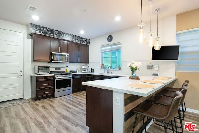 kitchen with pendant lighting, stainless steel appliances, a kitchen breakfast bar, kitchen peninsula, and dark brown cabinets