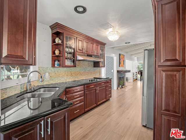 kitchen featuring light hardwood / wood-style flooring, black cooktop, stainless steel fridge, sink, and dark stone countertops