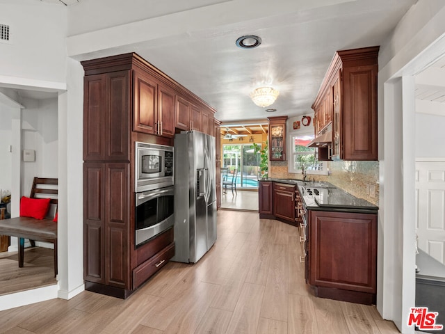 kitchen with light hardwood / wood-style floors, appliances with stainless steel finishes, dark stone counters, sink, and backsplash