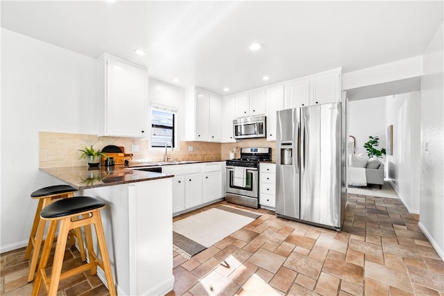 kitchen featuring white cabinets, appliances with stainless steel finishes, sink, a kitchen breakfast bar, and kitchen peninsula