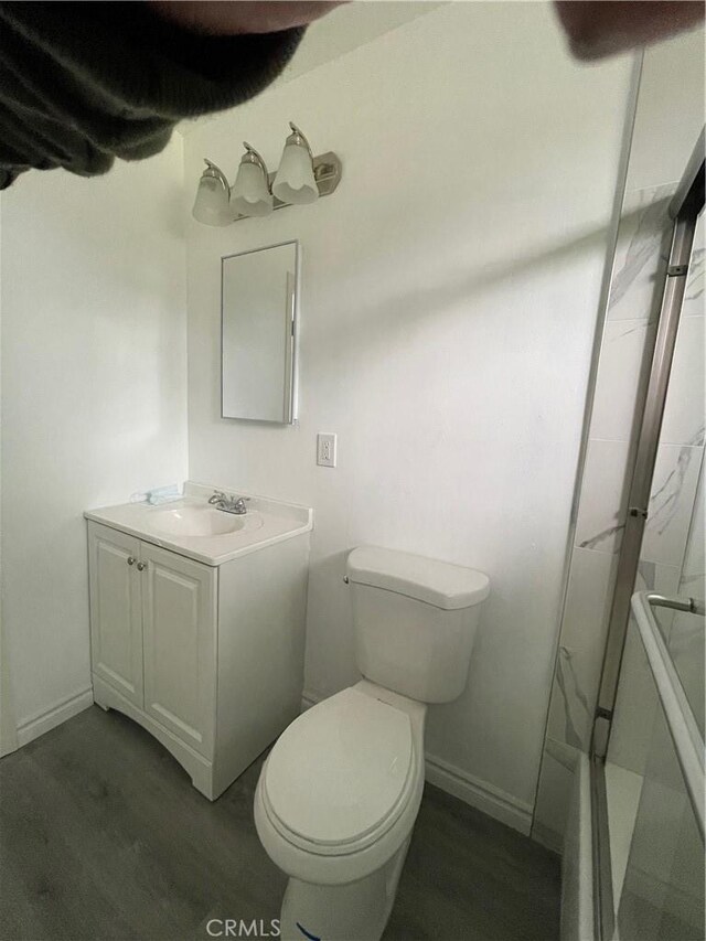 bathroom featuring wood-type flooring, toilet, vanity, and walk in shower