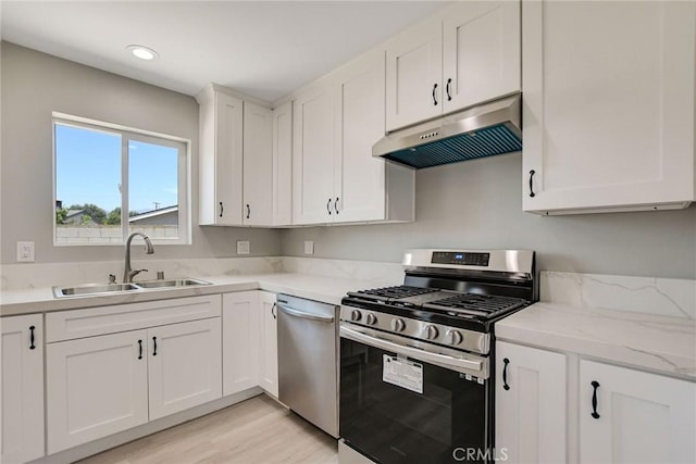 kitchen featuring stainless steel appliances, white cabinets, light stone countertops, light hardwood / wood-style flooring, and sink