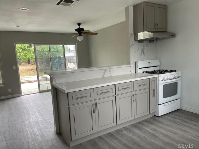 kitchen featuring exhaust hood, white range with gas cooktop, kitchen peninsula, ceiling fan, and light hardwood / wood-style flooring