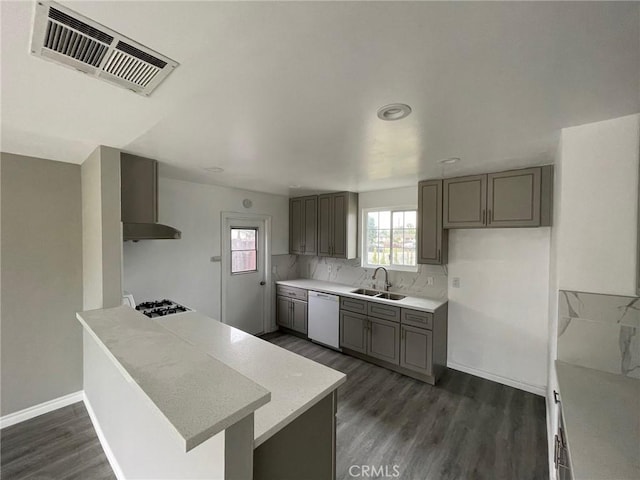 kitchen with gray cabinetry, gas stovetop, white dishwasher, wall chimney range hood, and sink