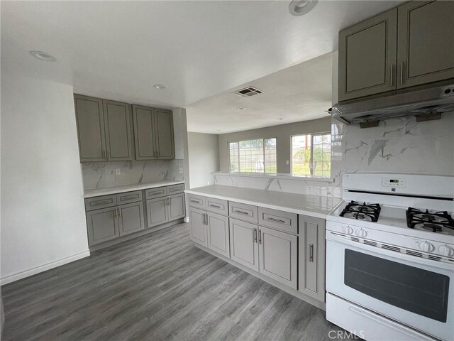 kitchen with tasteful backsplash, white gas stove, gray cabinets, kitchen peninsula, and hardwood / wood-style flooring