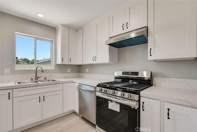 kitchen with white cabinetry, stainless steel appliances, light wood-type flooring, light stone counters, and sink