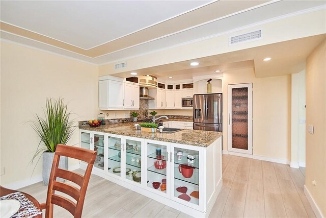 kitchen with sink, white cabinets, light stone counters, kitchen peninsula, and stainless steel appliances