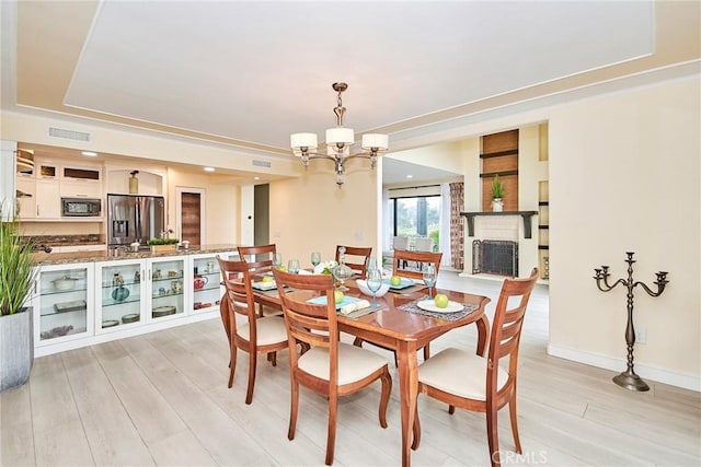 dining space with a tray ceiling, a brick fireplace, a notable chandelier, and light hardwood / wood-style flooring