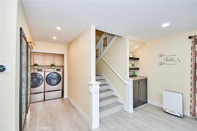 clothes washing area featuring cabinets, washing machine and dryer, and light hardwood / wood-style floors