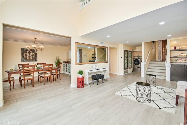 living room featuring a notable chandelier, recessed lighting, light wood-style flooring, washer / dryer, and stairs