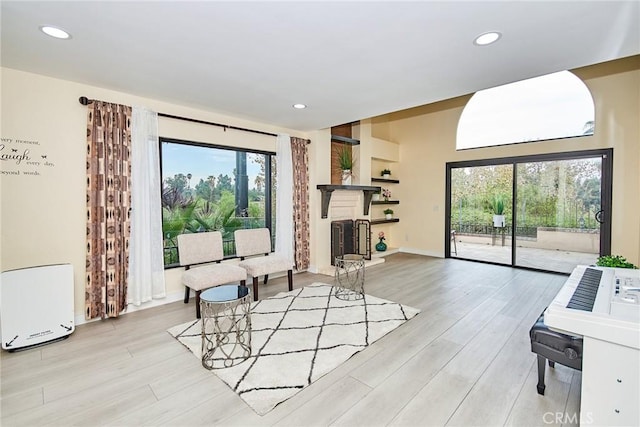 sitting room with light wood-style flooring, baseboards, a fireplace with raised hearth, and recessed lighting