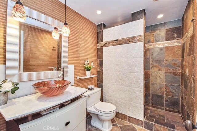 bathroom featuring vanity, a shower, toilet, and tile walls