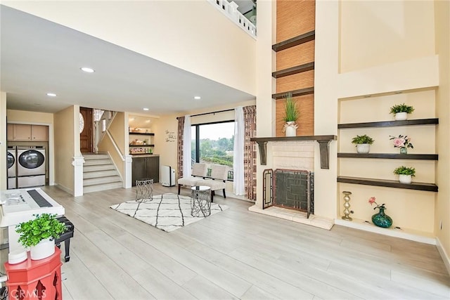 living room with washer and dryer, a high ceiling, a brick fireplace, light wood-type flooring, and built in shelves