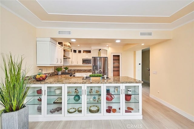 kitchen with light stone counters, kitchen peninsula, stainless steel appliances, light hardwood / wood-style floors, and white cabinets