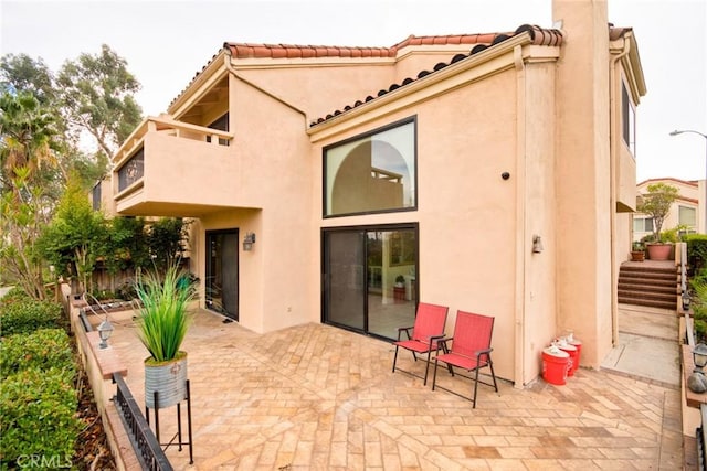 rear view of house with fence, a patio, a tiled roof, and stucco siding