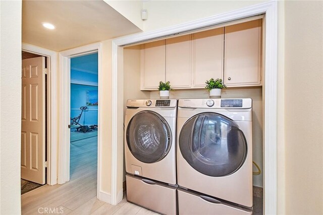 clothes washing area with cabinets, washing machine and clothes dryer, and light wood-type flooring