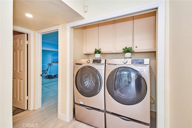 clothes washing area featuring washing machine and clothes dryer, cabinet space, and light wood-style floors