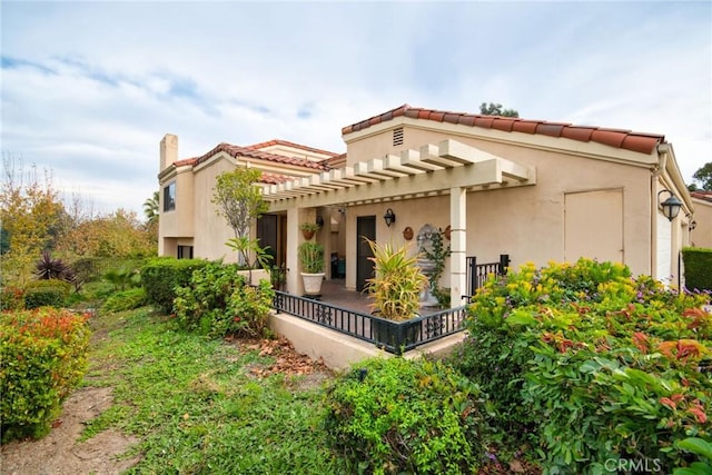 view of side of home featuring a chimney, stucco siding, a tile roof, and a pergola