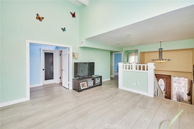 living room featuring light wood-type flooring, a high ceiling, and baseboards