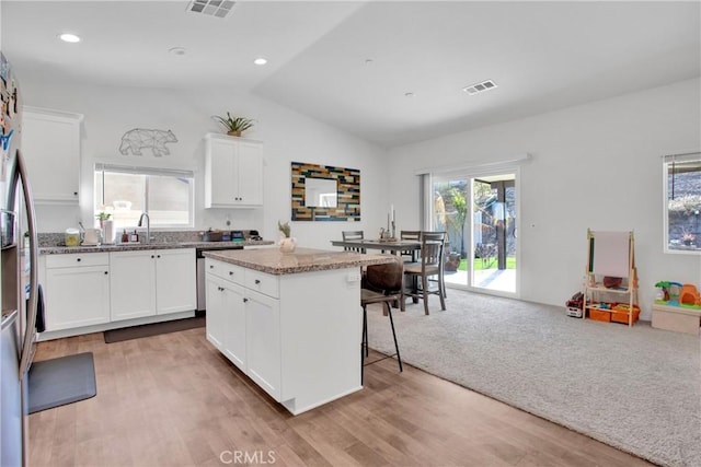 kitchen featuring white cabinets, a center island, vaulted ceiling, light stone counters, and a breakfast bar area