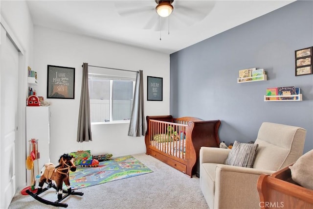 carpeted bedroom with ceiling fan and a crib