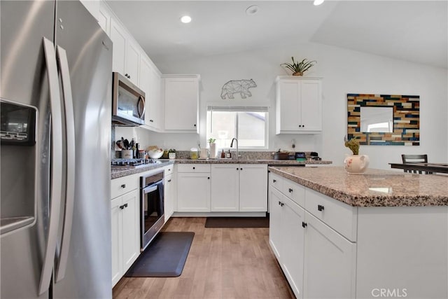 kitchen with white cabinetry, light hardwood / wood-style floors, stainless steel appliances, lofted ceiling, and light stone counters