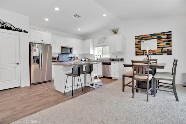 kitchen with vaulted ceiling, stainless steel appliances, white cabinets, and a kitchen island