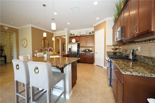 kitchen featuring appliances with stainless steel finishes, pendant lighting, dark stone countertops, and a kitchen island with sink