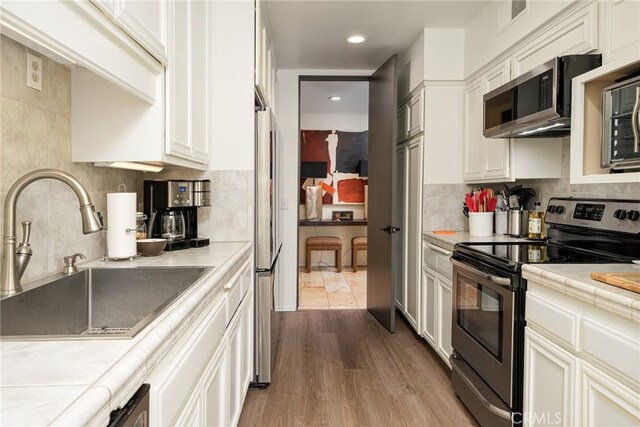 kitchen with tile countertops, stainless steel appliances, light hardwood / wood-style flooring, and sink