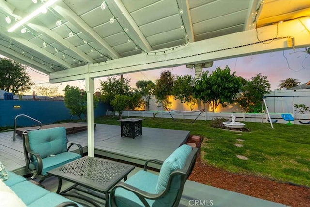 patio terrace at dusk with a deck, an outdoor living space, and a lawn