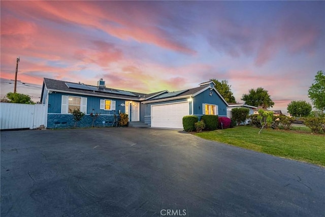 single story home with a garage, a lawn, and solar panels