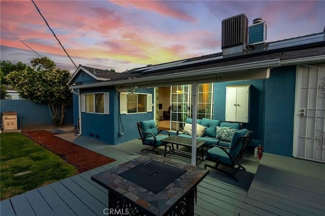 back house at dusk with a deck, an outdoor living space with a fire pit, cooling unit, and solar panels