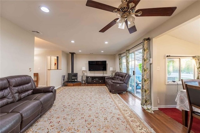 living room featuring ceiling fan, vaulted ceiling, a wood stove, and hardwood / wood-style flooring