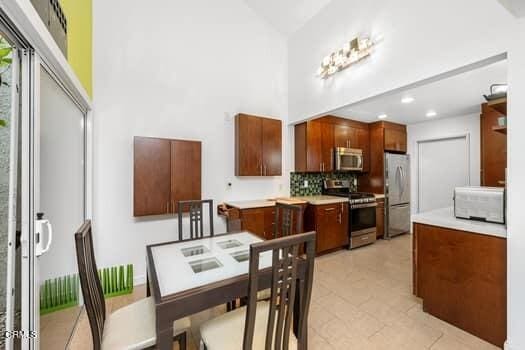 kitchen with light tile patterned flooring, stainless steel appliances, decorative backsplash, and a high ceiling