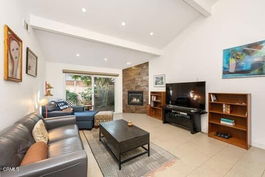 living room featuring lofted ceiling with beams and a stone fireplace