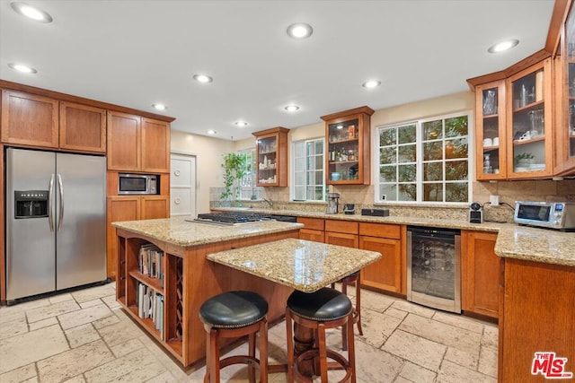 kitchen with a breakfast bar, wine cooler, light stone countertops, a kitchen island, and stainless steel appliances